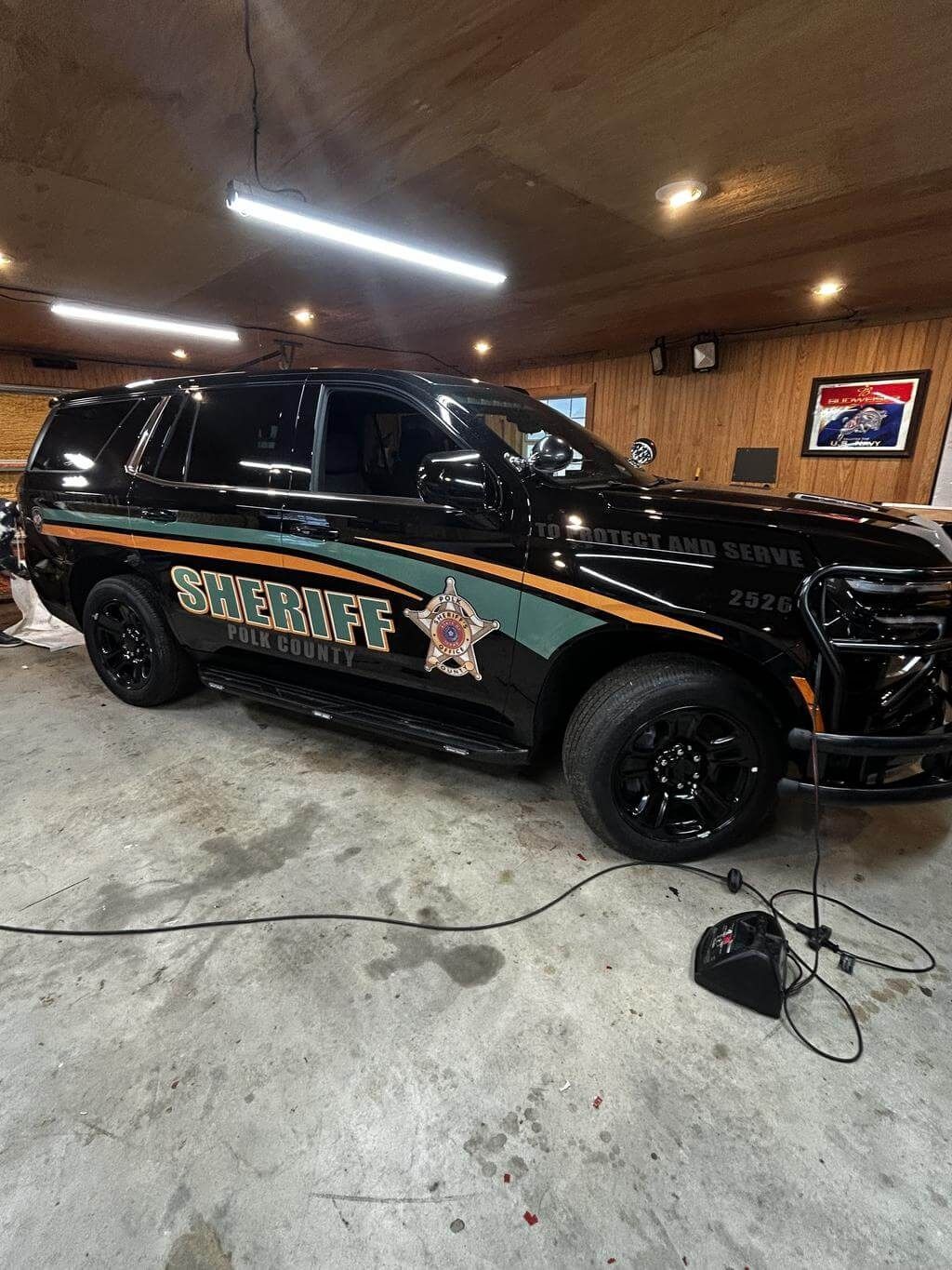 Black SUV with sheriff-style decals parked in a garage with wood-paneled walls.