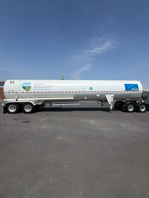 White tanker truck parked on asphalt under a blue sky, side view with company logos and markings