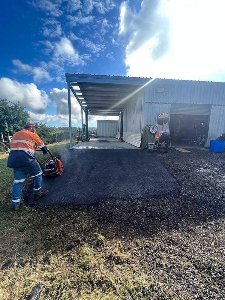 A Man Is Using A Lawn Mower To Cut Grass In Front Of A Building— Elite Bitumen & Asphalt In Mackay, QLD
