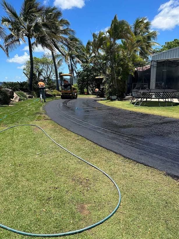 A Road Is Being Paved In Front Of A House With Palm Trees — Elite Bitumen & Asphalt In Mackay, QLD