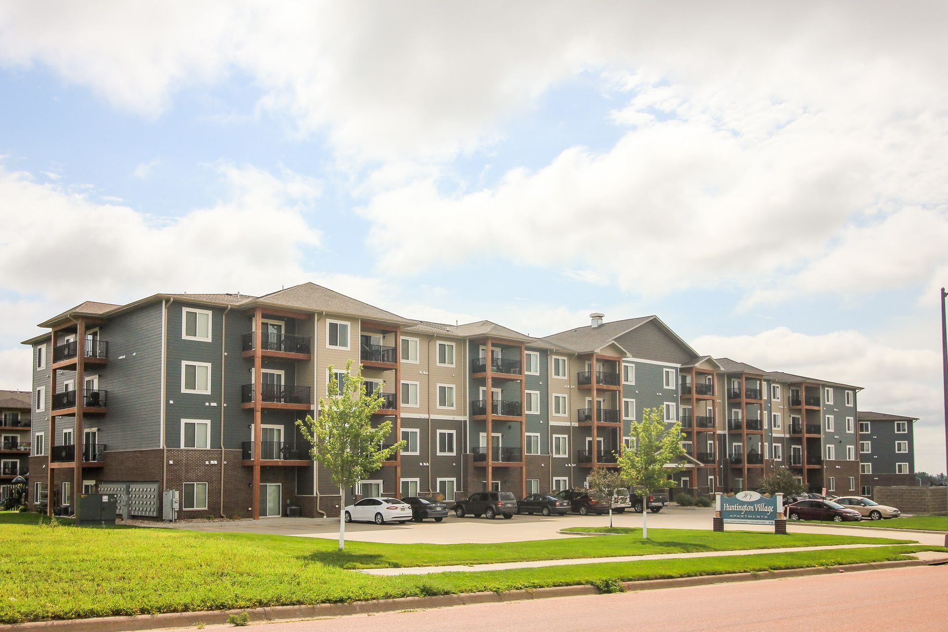 Apartment building with multiple stories and balconies, exterior view under a cloudy sky. Green lawn in the foreground.