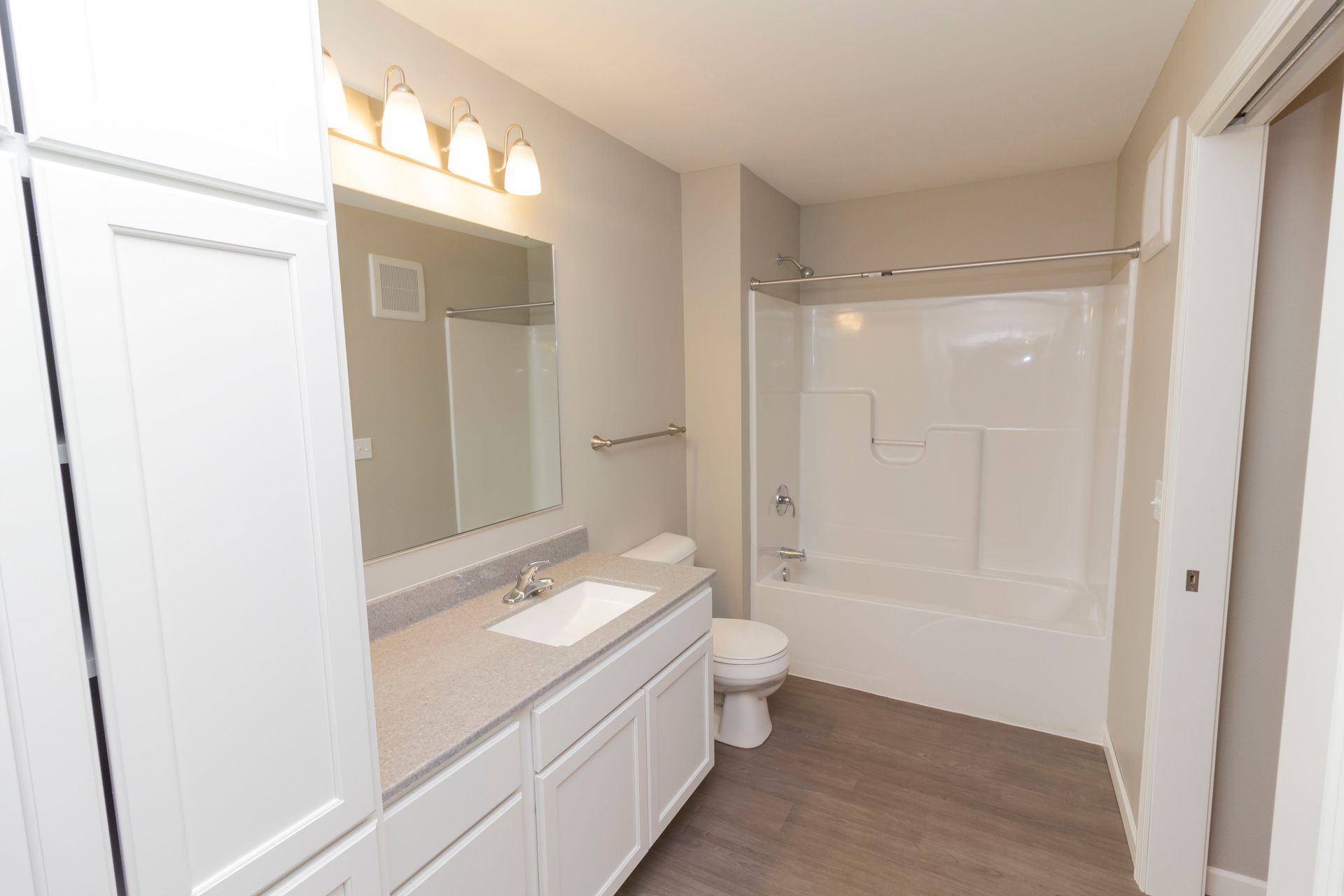 Bathroom with white cabinetry, a gray countertop, and a white tub. The floor is wood-look, and the walls are gray.