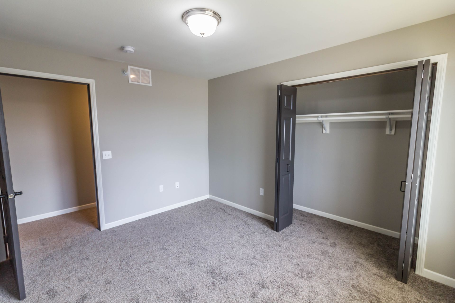 Empty bedroom with gray walls, carpet, and closet. The door is open to another room.