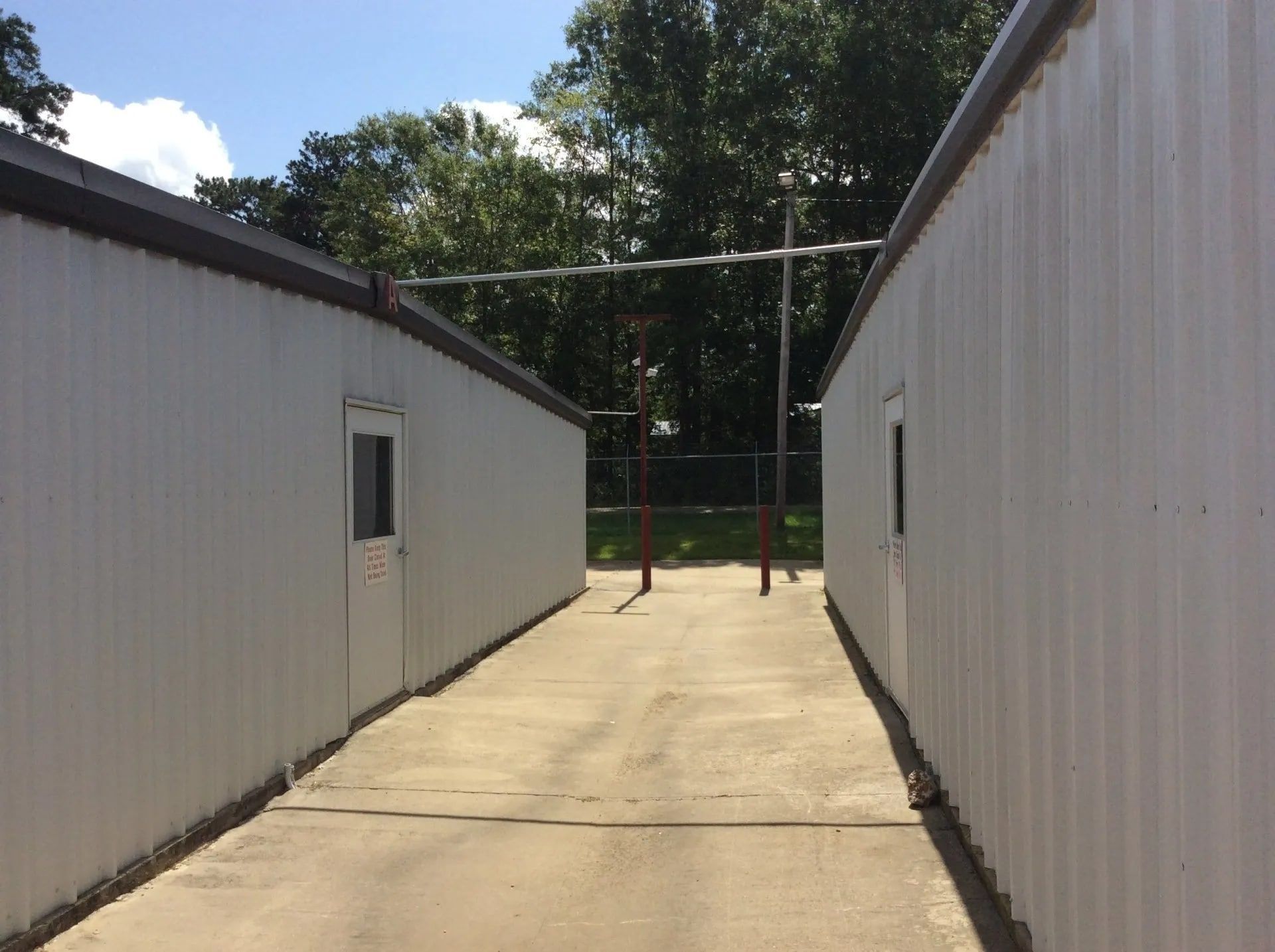 Two white buildings face each other, with a paved walkway between them. A metal bar structure stands in the distance.