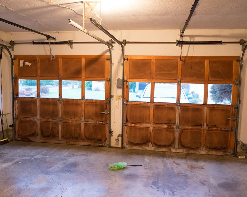 An empty garage with a wooden garage door and a green duster on the floor.