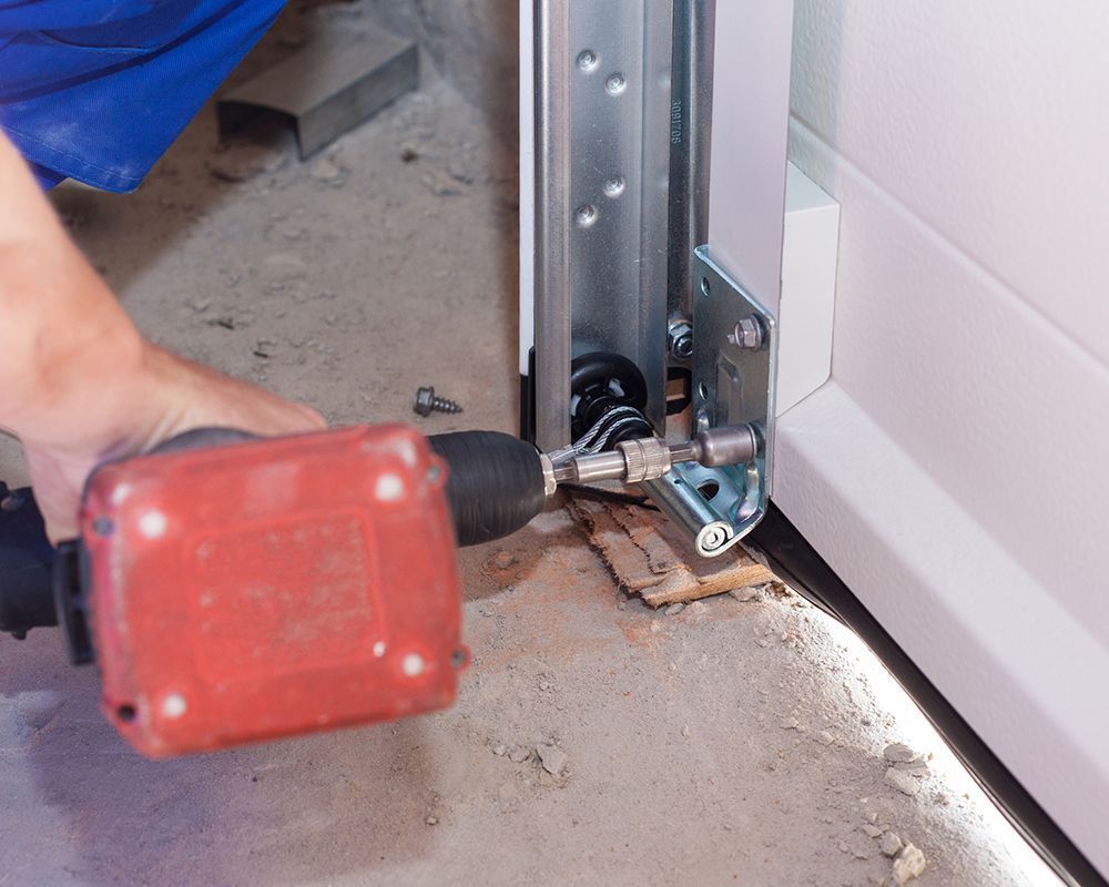 A person is using a drill to fix a garage door.