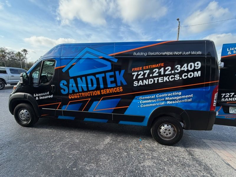 Sandtek Construction Services van with blue, black, and orange logo; parked outdoors.