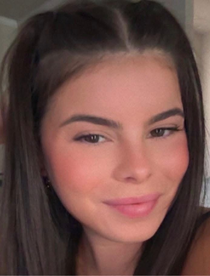 Woman with dark hair, smiling, wearing makeup.