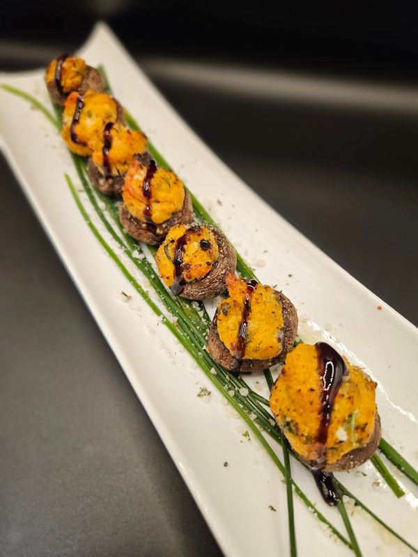 Stuffed mushrooms drizzled with balsamic glaze, served with a salad on a white plate.