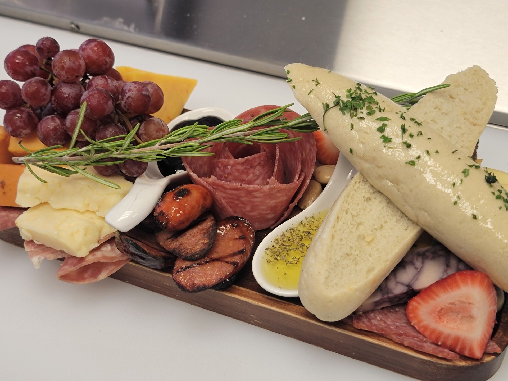 Meat and cheese with grapes, cheese, meats, bread, and a sprig of rosemary.