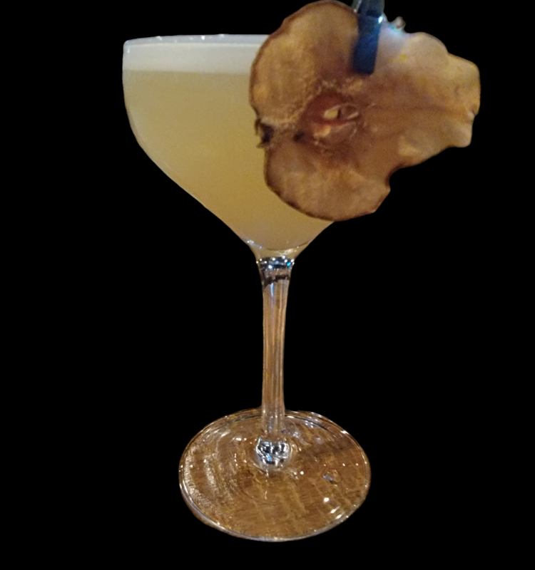 Cocktail in a stemmed glass, garnished with a dried apple slice, against a black background.