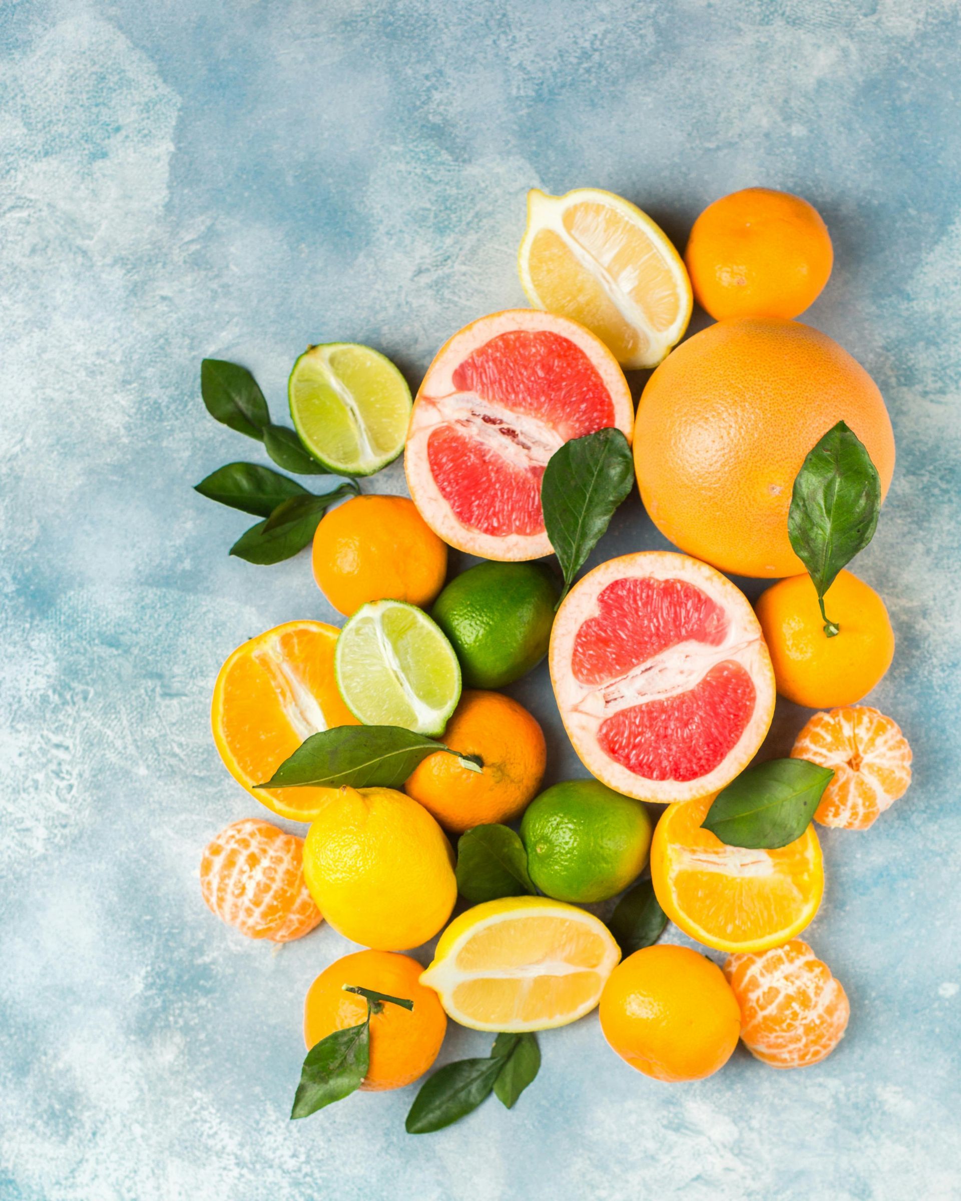 Assortment of citrus fruits, including grapefruit, lemons, limes, and tangerines, on a blue textured surface.