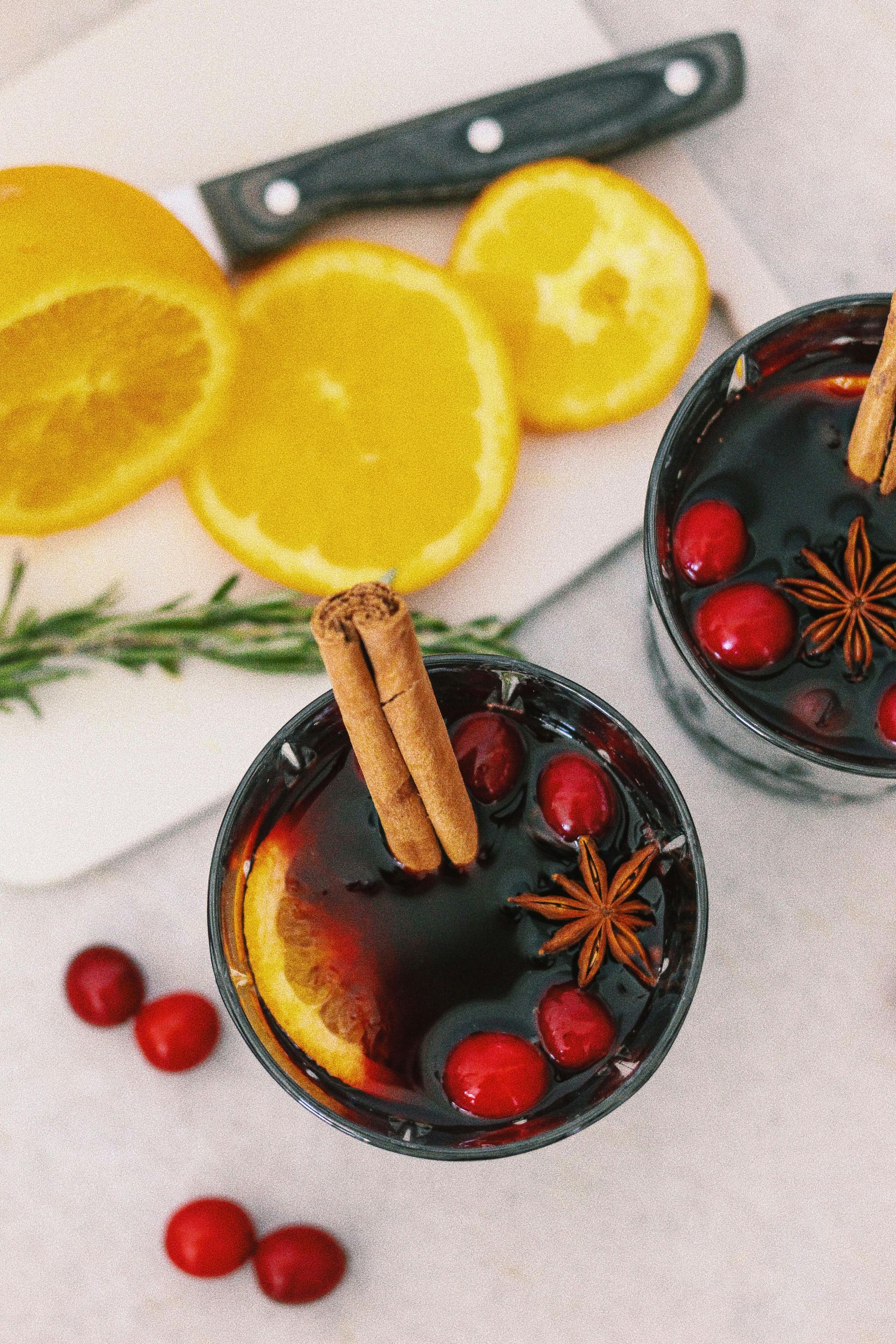 Mulled wine in mugs, garnished with cranberries, orange slices, and cinnamon.