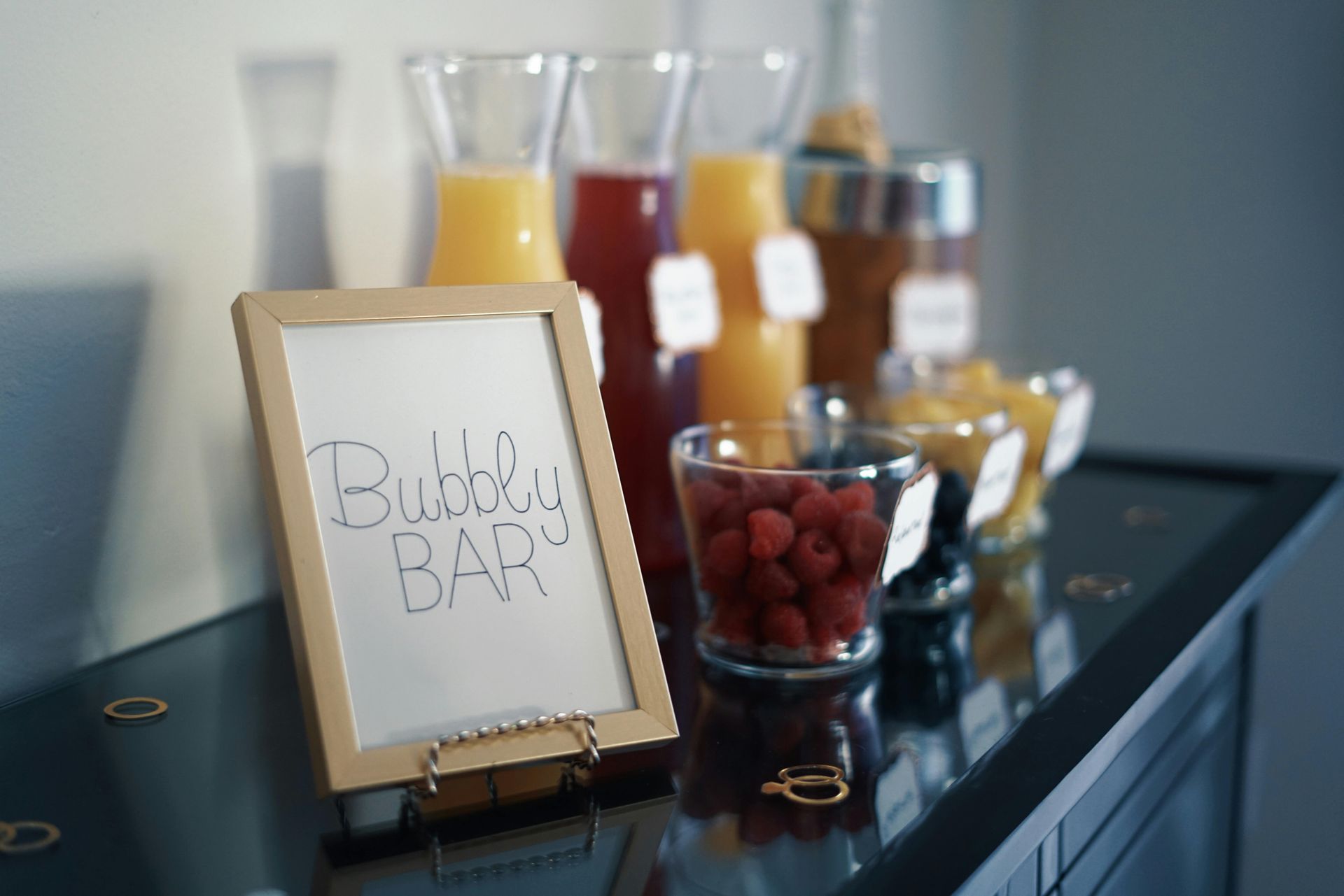 Bubbly bar with various juices, berries, and a sign.