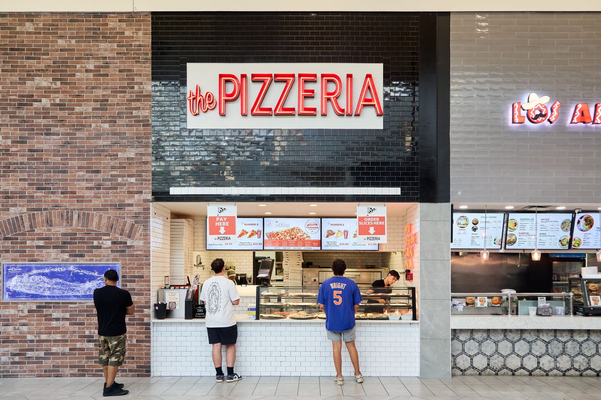 A man is standing behind a counter at a pizza restaurant.