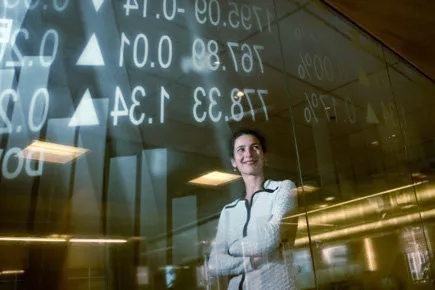 A woman is standing in front of a glass wall with her arms crossed.