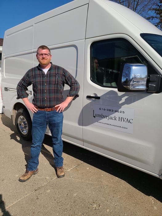 A man in a plaid shirt is standing in front of a white van.