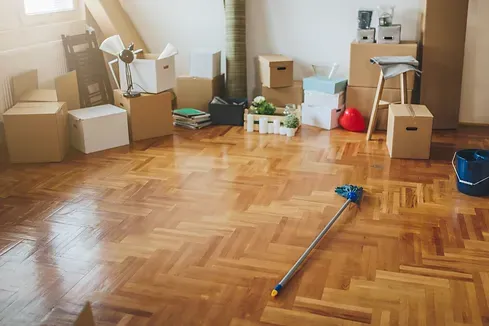 Room with wooden floor and moving boxes, mop on the floor.
