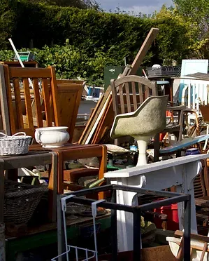Pile of various used furniture items outside, including chairs, tables, and wooden planks.