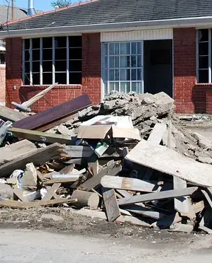 Pile of debris in front of a brick building with broken windows and an open doorway.