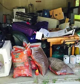 A pile of luggage is sitting in a garage next to bags of earthys