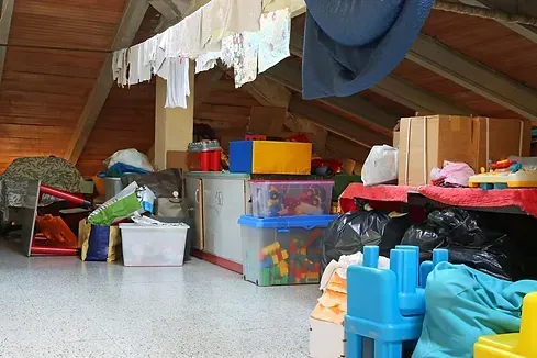 Cluttered attic storage space with various boxes, bags, and laundry drying overhead.