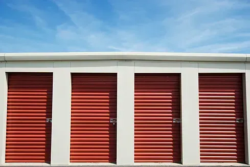 Four red storage unit doors against a blue sky.