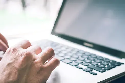 Hands typing on a laptop keyboard near a window with sunlight.