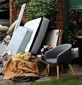 A pile of mattresses , blankets , chairs , and other items in front of a house.