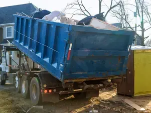 A dumpster truck is being loaded with garbage in front of a house.