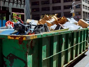 A green dumpster filled with lots of trash on the side of the road.