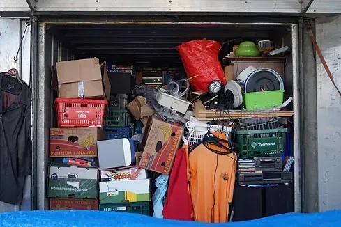 A storage unit filled with various packed boxes, crates, and items; orange, red and green items visible.