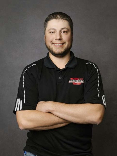 Man in black polo shirt with arms crossed, smiling, standing in front of a gray backdrop.
