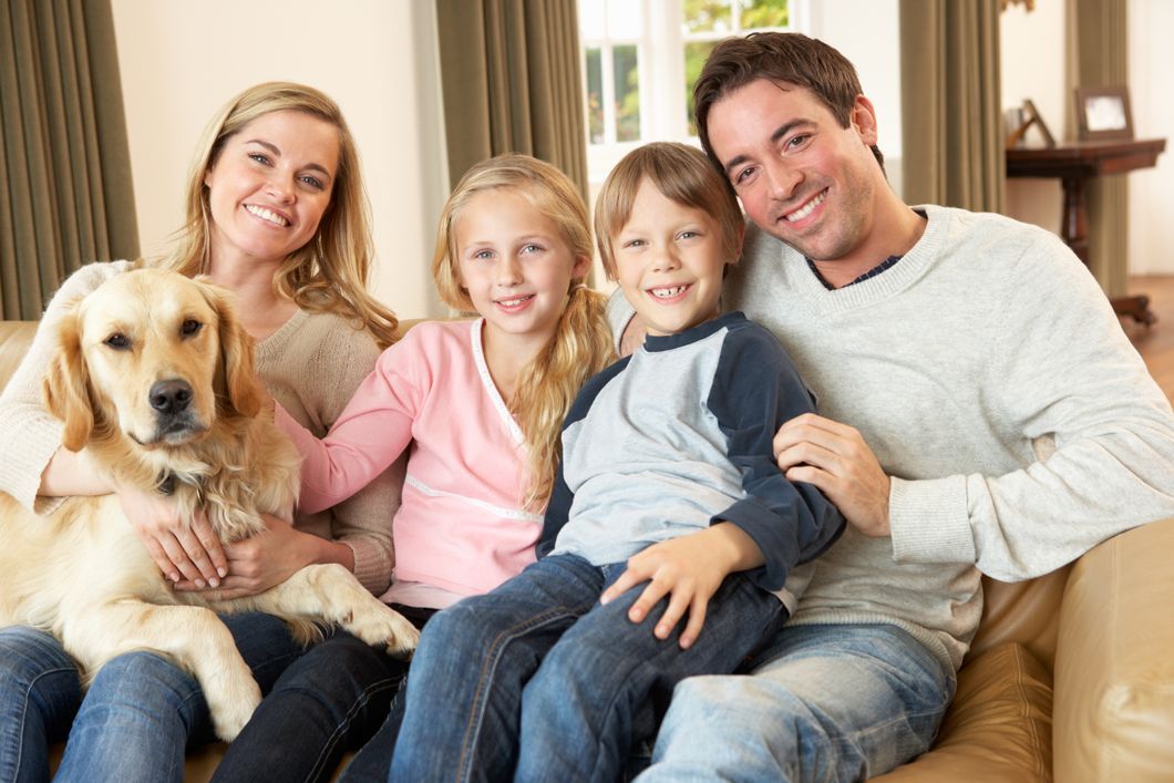 Family of four and a dog smiling on a couch in a living room.