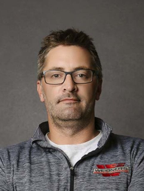 Man with glasses in a gray zip-up sweatshirt, against a gray background.