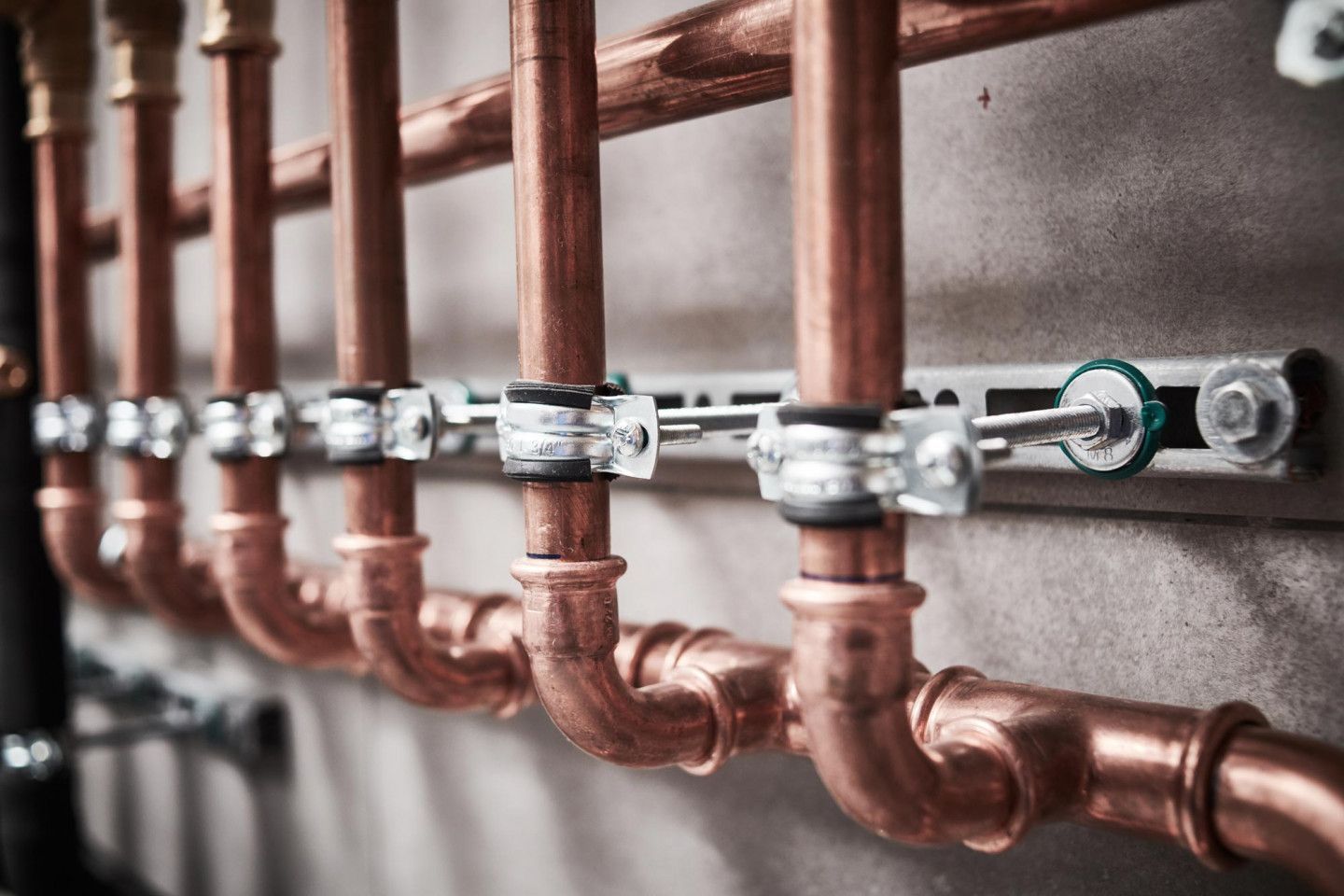 Copper pipes secured to a wall with metal clamps.