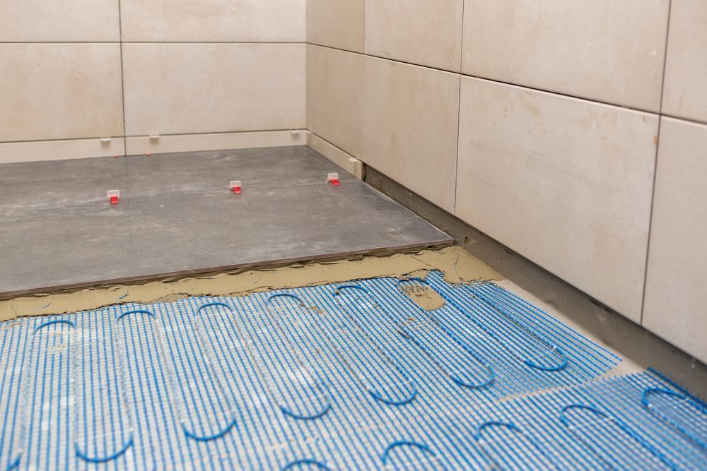 Bathroom floor with blue radiant heat mat, concrete layer, and tile installation in progress.