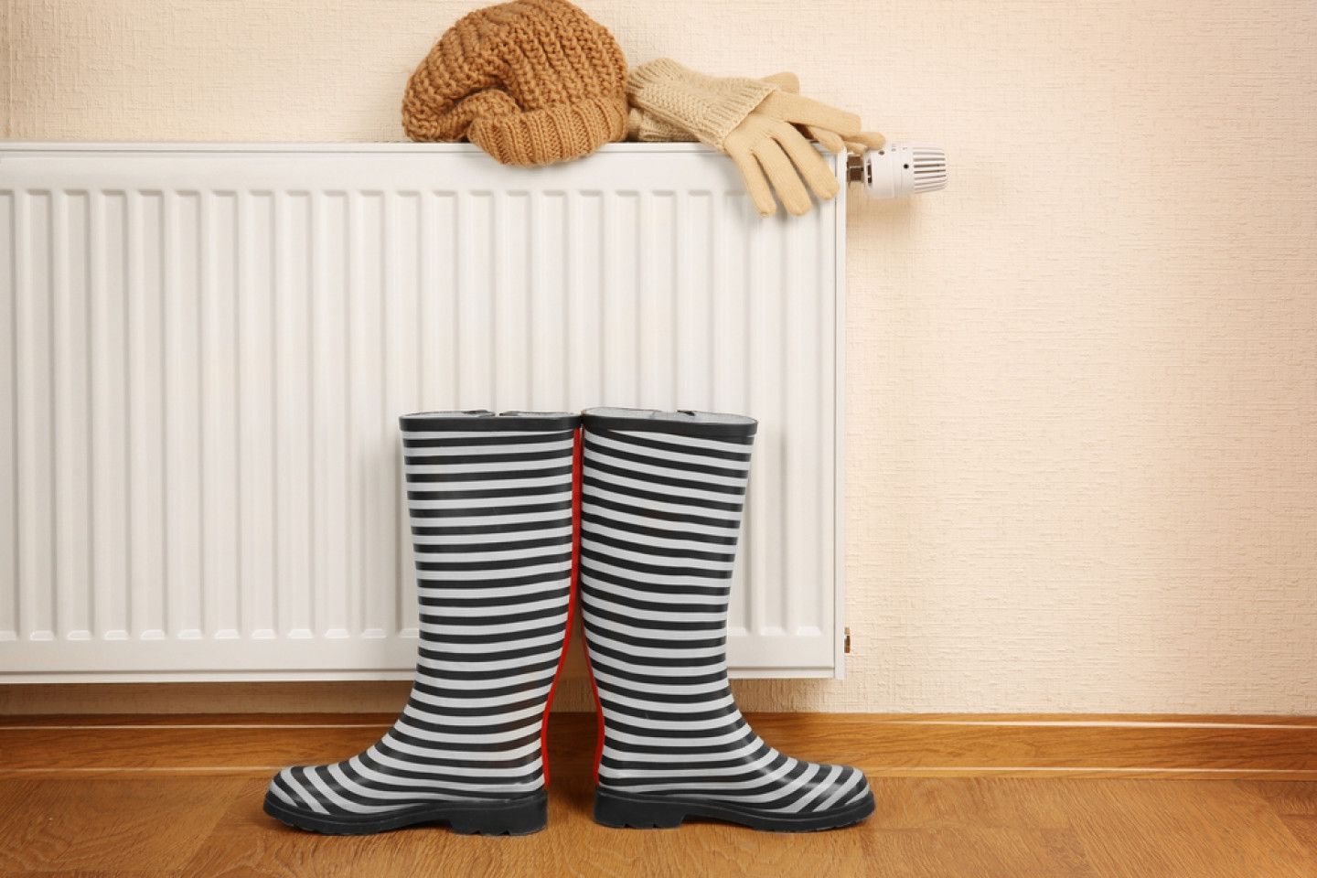 Pair of rain boots and winter hat and gloves drying on a radiator.