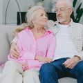 Older couple sitting on a couch, smiling at each other in a bright living room