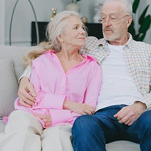 Older couple sitting on a couch, smiling at each other in a bright living room