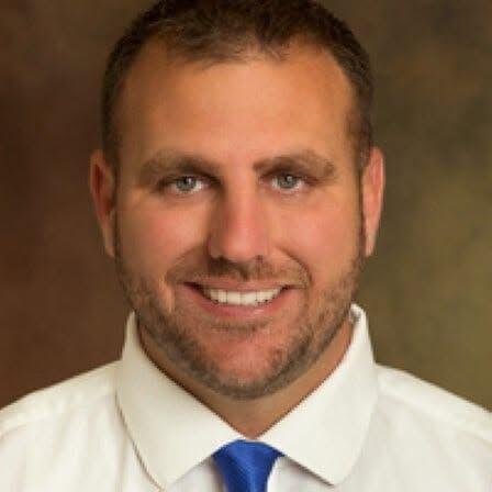 Smiling man in white shirt and blue tie against a brown background