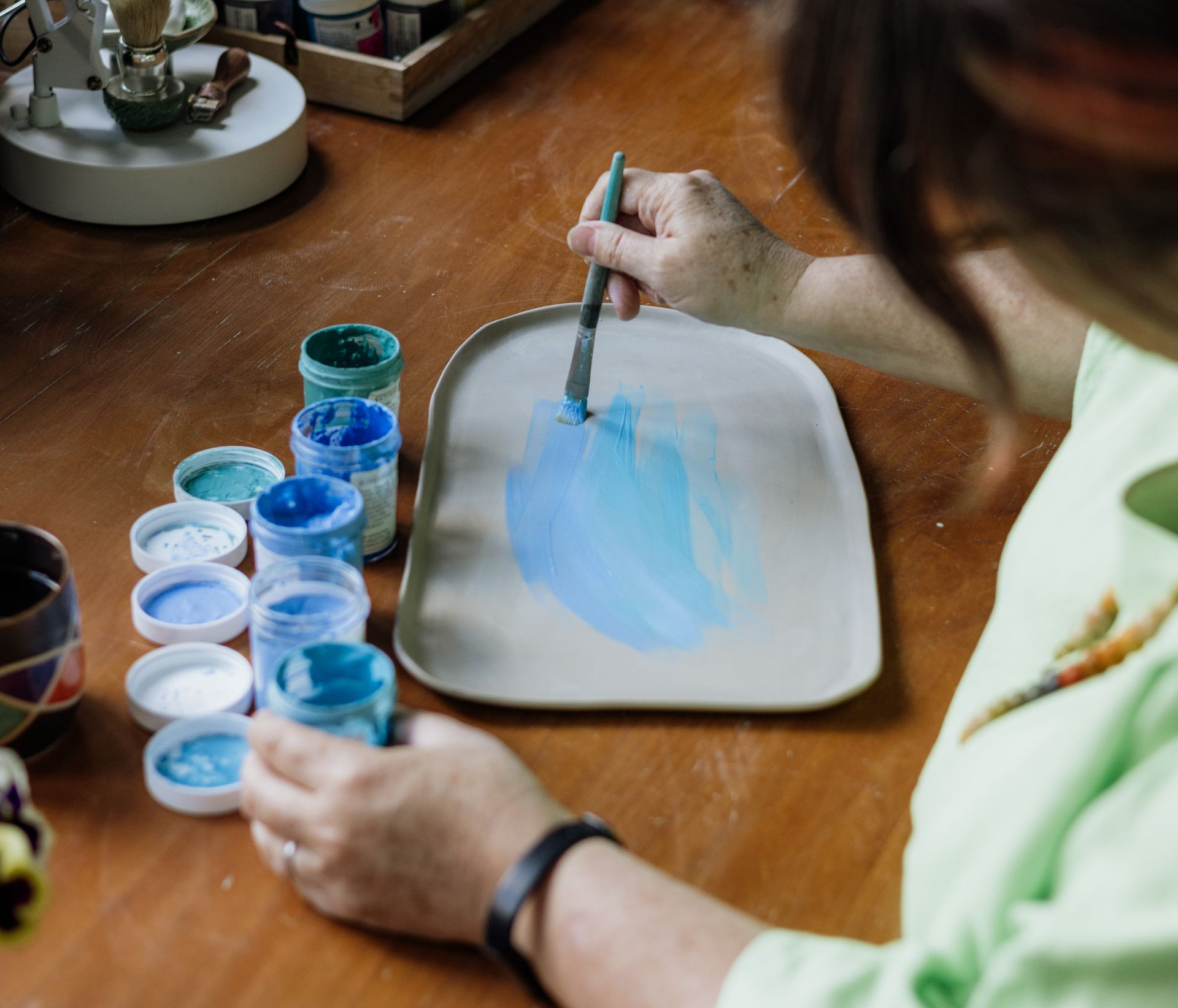 Artist's hand painting blue tones of underglaze on a clay platter.