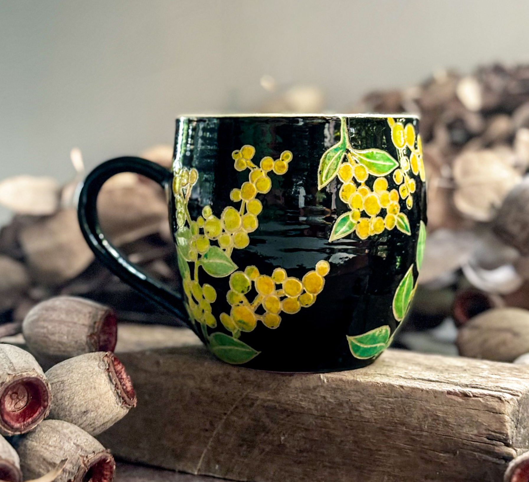 A handmade mug with a black background and sprays of yellow wattle flowers