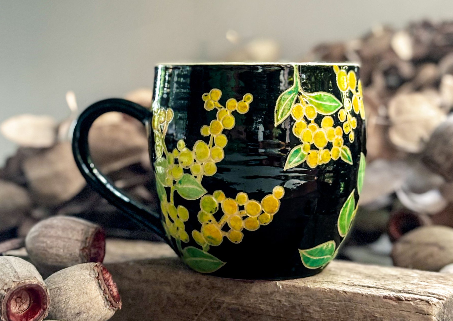 A handmade mug with a black background and sprays of yellow wattle flowers