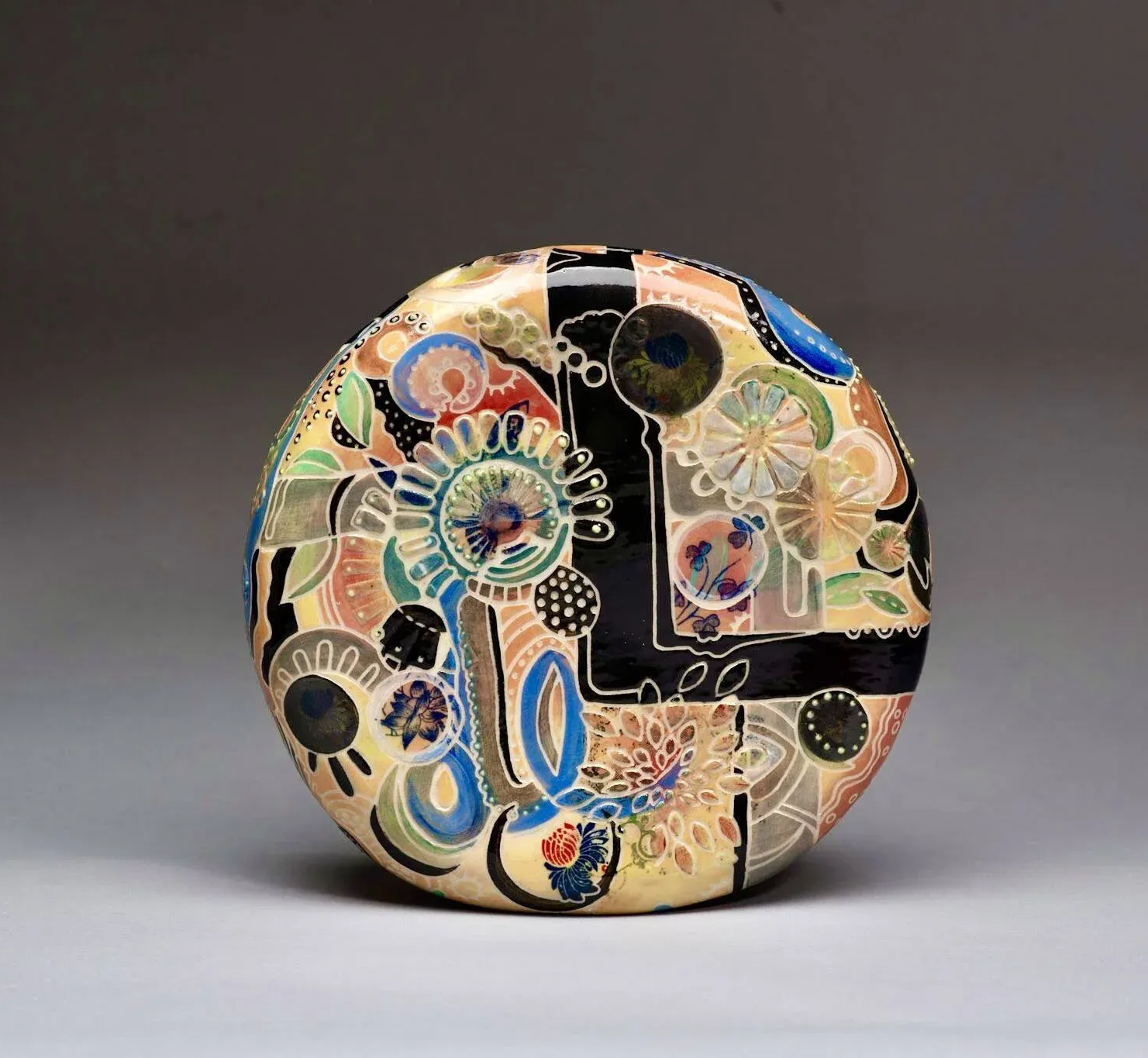 Circular, patterned decorative box; black stripes, colorful floral and abstract designs on cream.