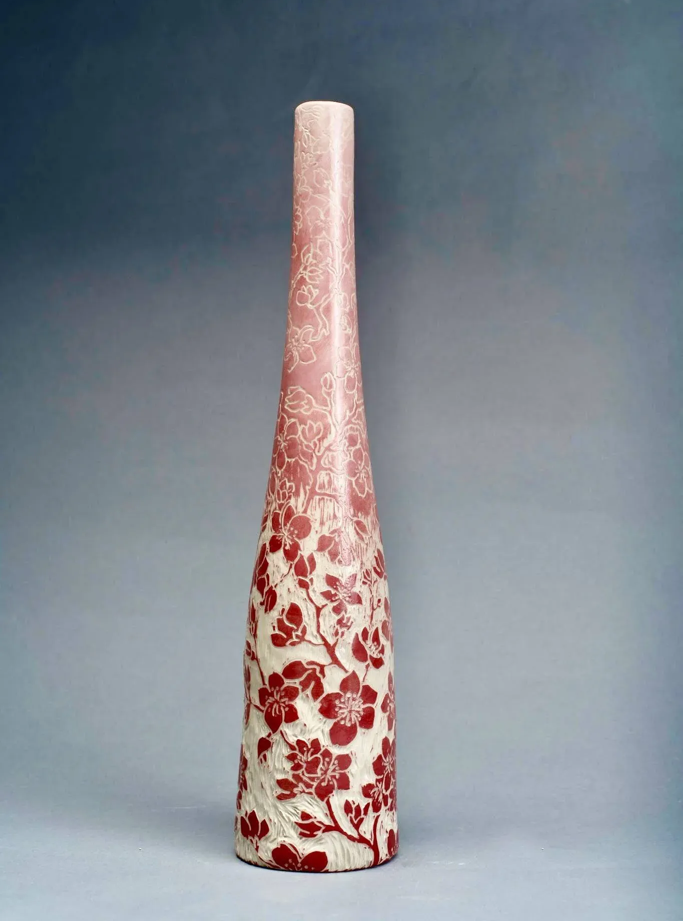 Tall, tapered vase with a floral pattern in red on a cream background, fading to solid pink.