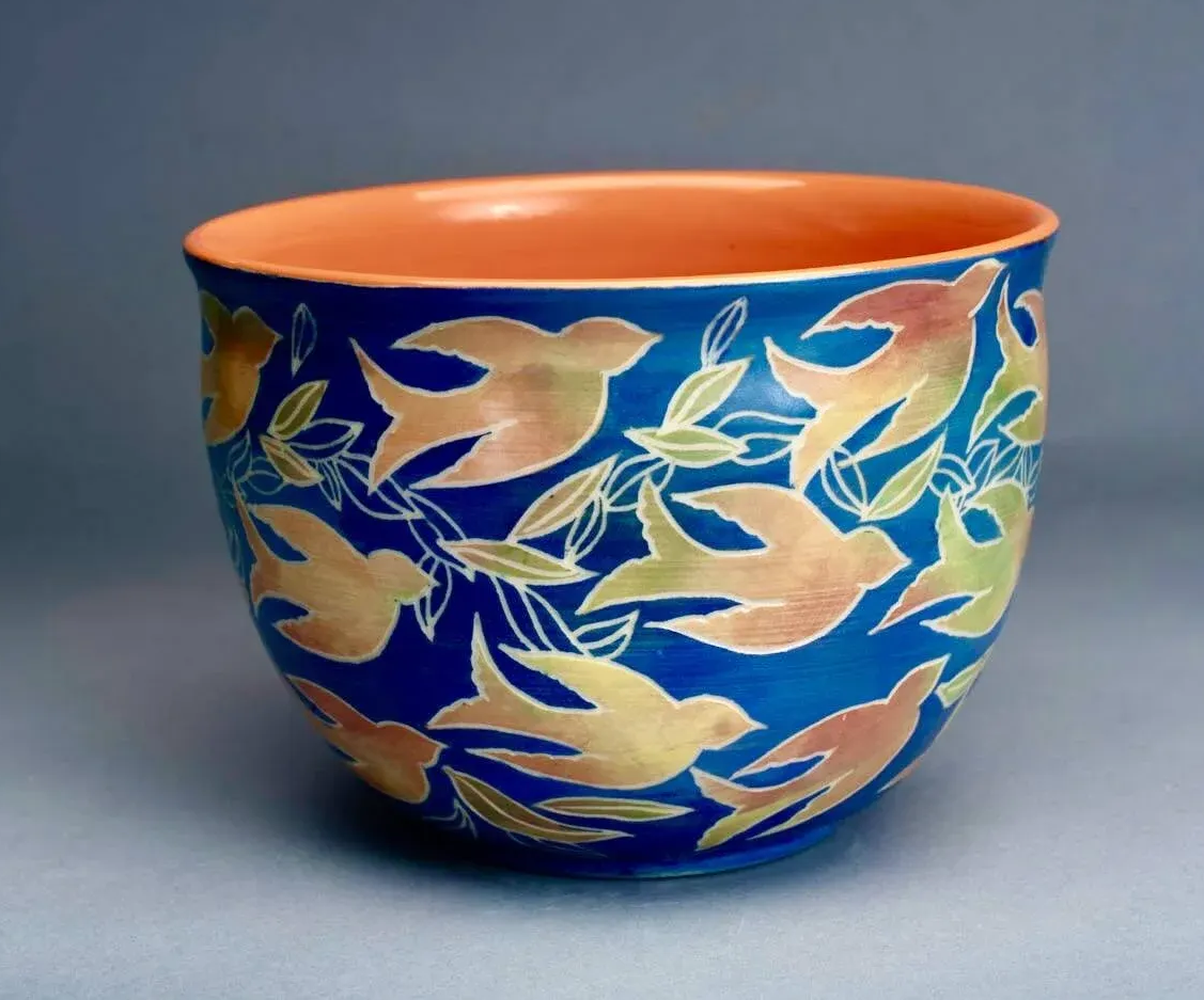 Ceramic bowl with birds flying around against a blue background and with an orange interior.