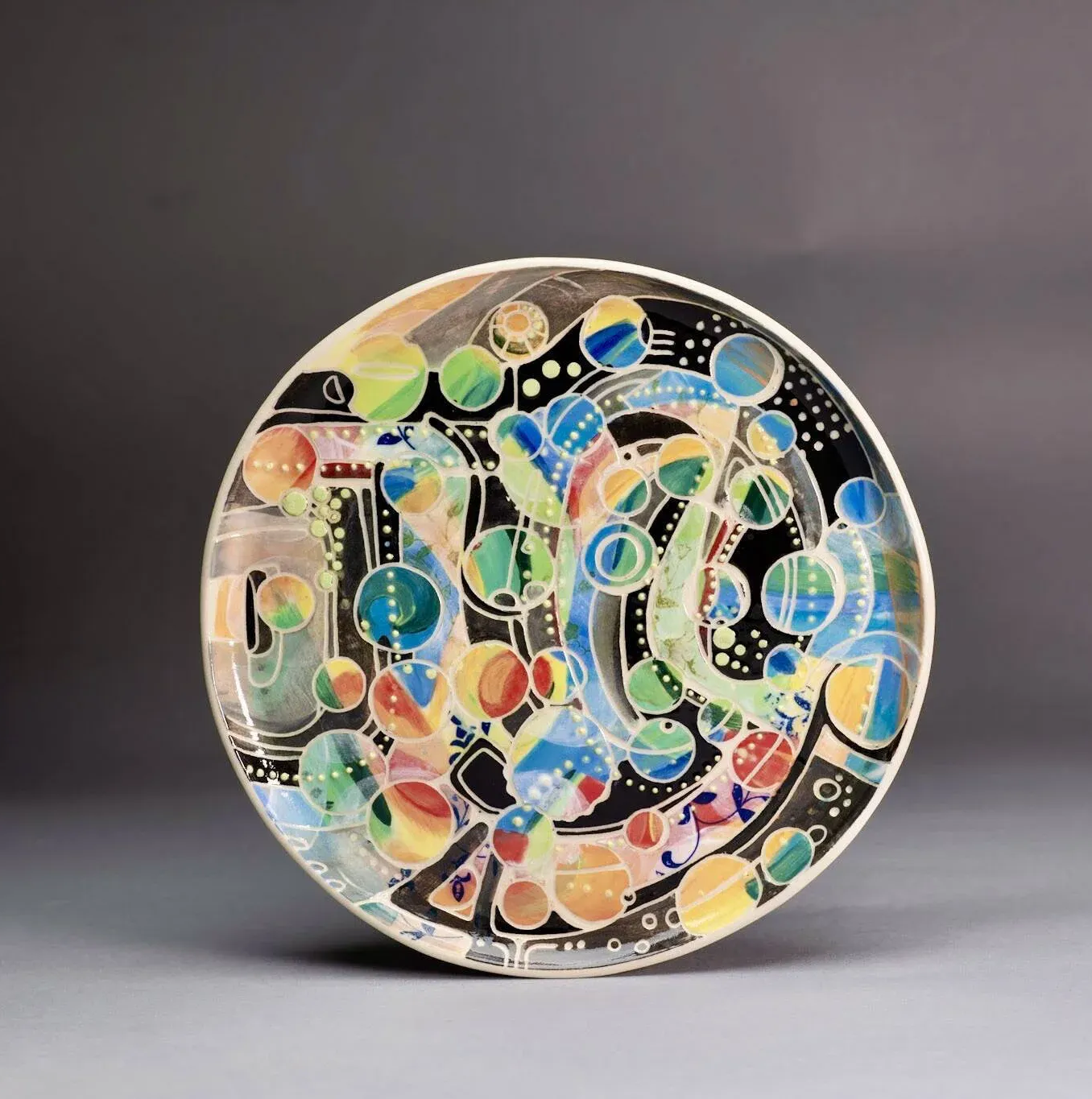 Colorful abstract design on a round plate; black background with blues, greens, and yellows.