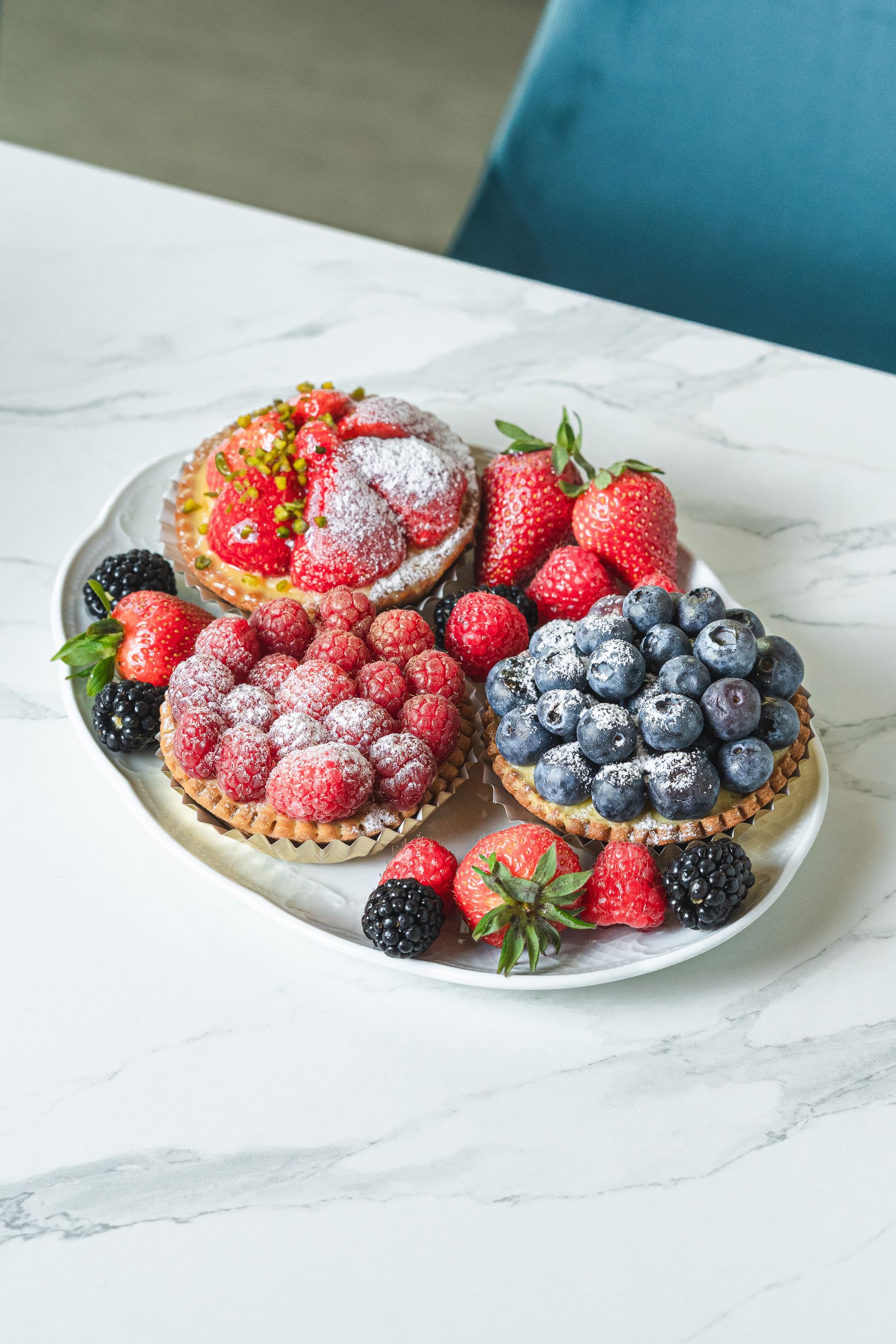 Assiette de fruits rouges et de pâtisseries assorties saupoudrées de sucre glace sur une table en marbre