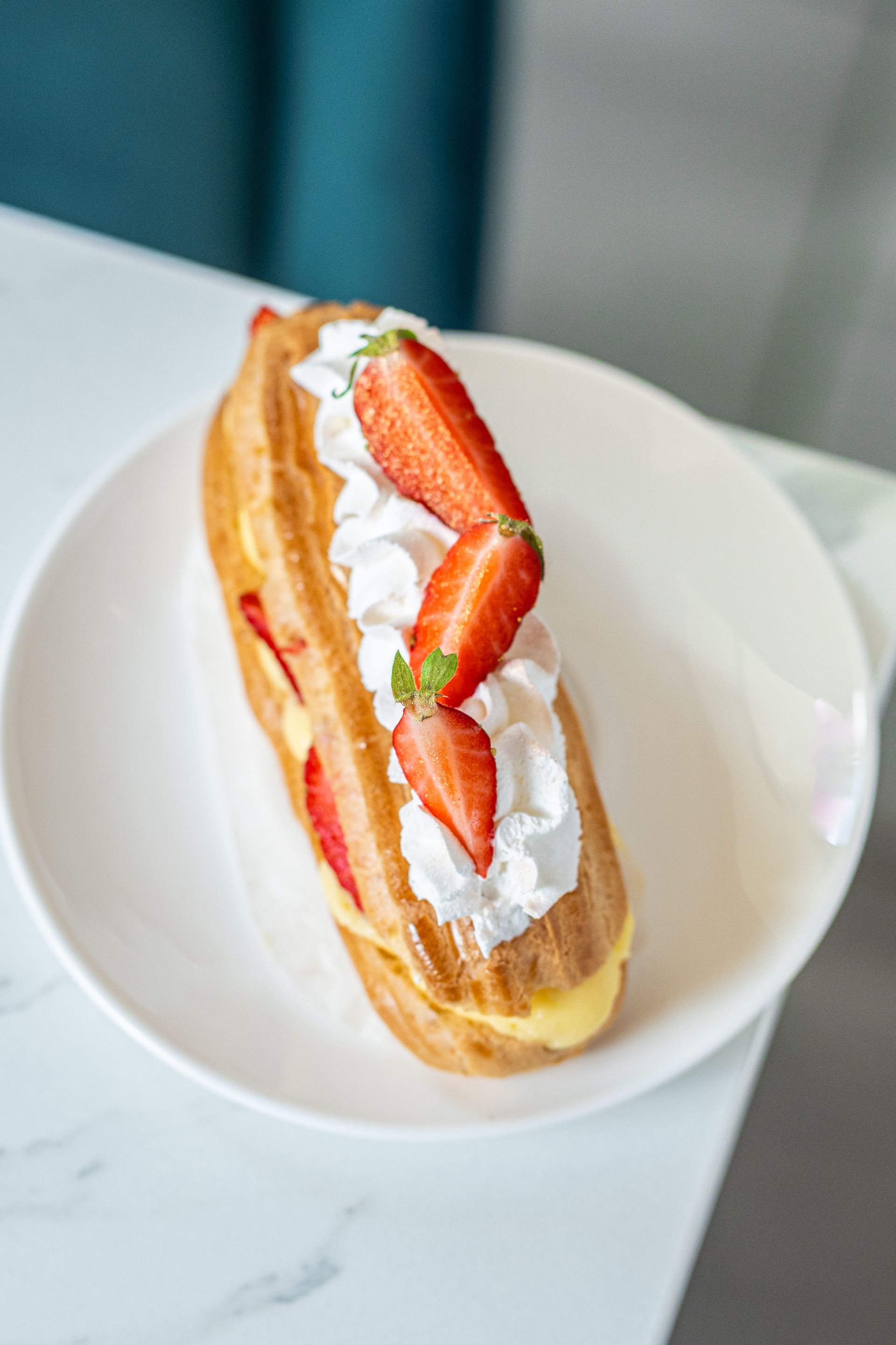 Pâtisserie à la crème de fraises sur une assiette blanche, garnie de crème fouettée et de fraises tranchées.